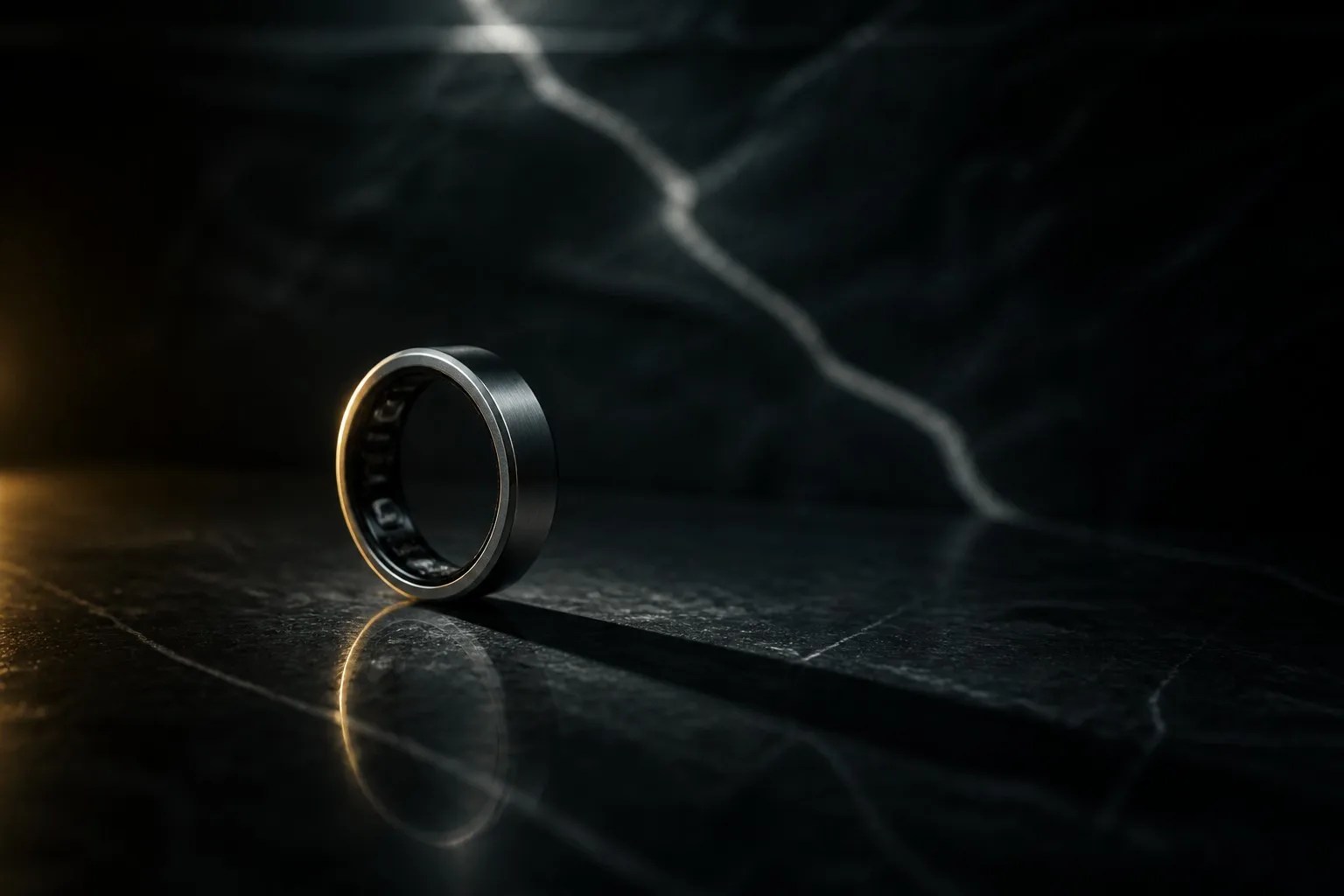 A single titanium smart ring standing upright on black polished stone, casting a long shadow
