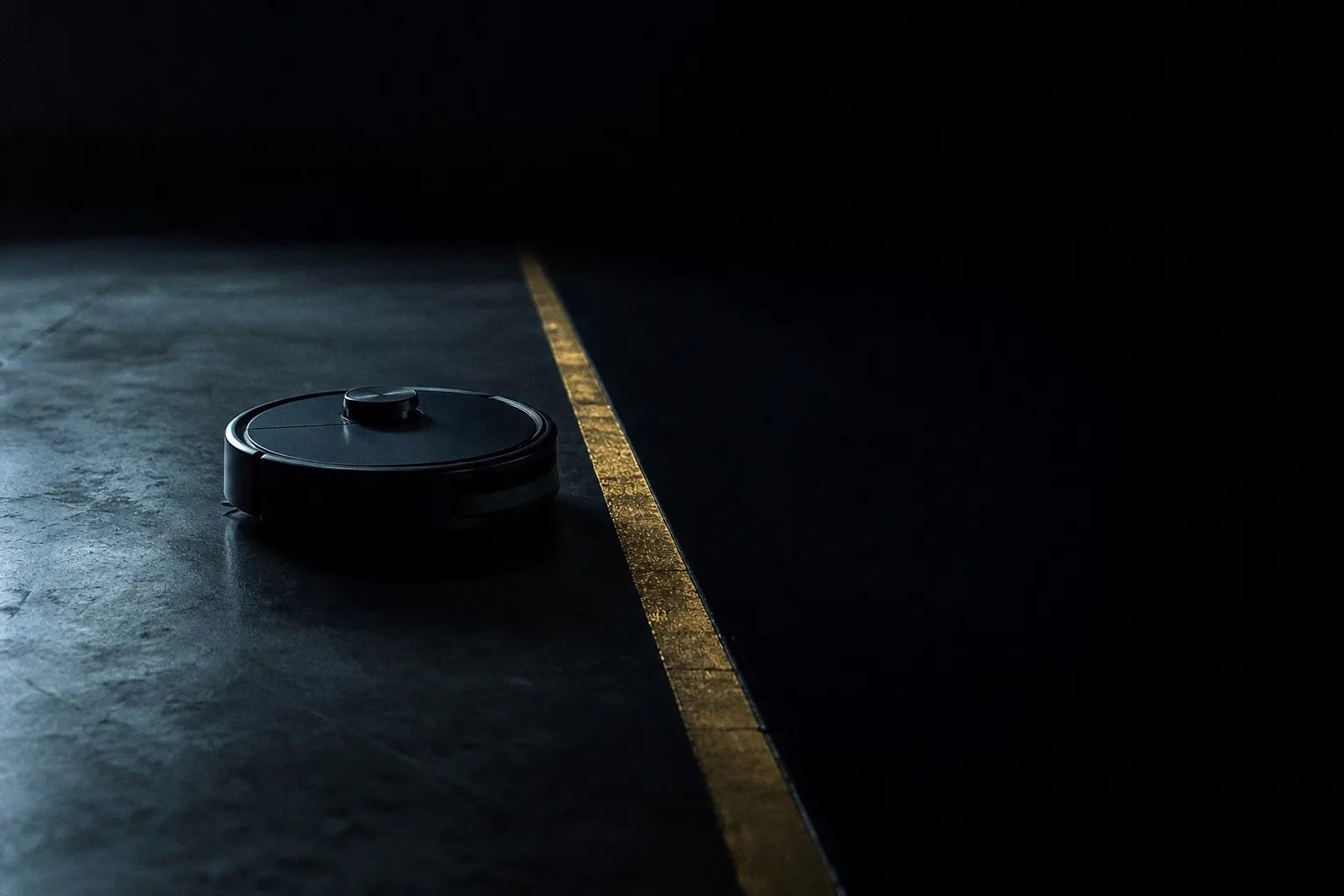 A small robot vacuum stopped at a glowing boundary line on a dark concrete floor