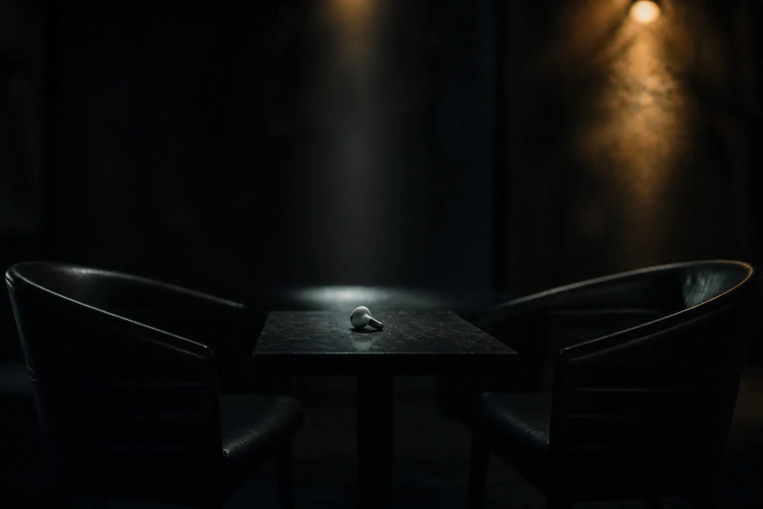 Two empty chairs facing each other across a dark table with a single earbud between them